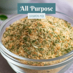 A small glass bowl of homemade all-purpose seasoning mix surrounded by salt, pepper, garlic, and onion powder on a cozy kitchen counter in natural daylight.
